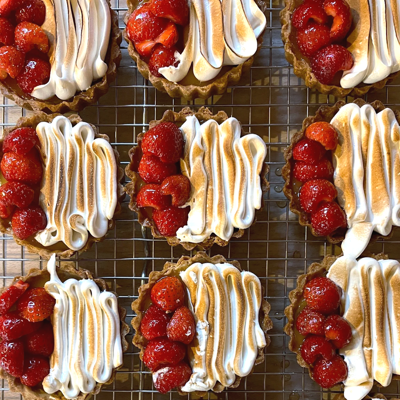 Overhead view of Lemon Tarts topped with torched Swiss meringue and strawberries on a cooling rack.