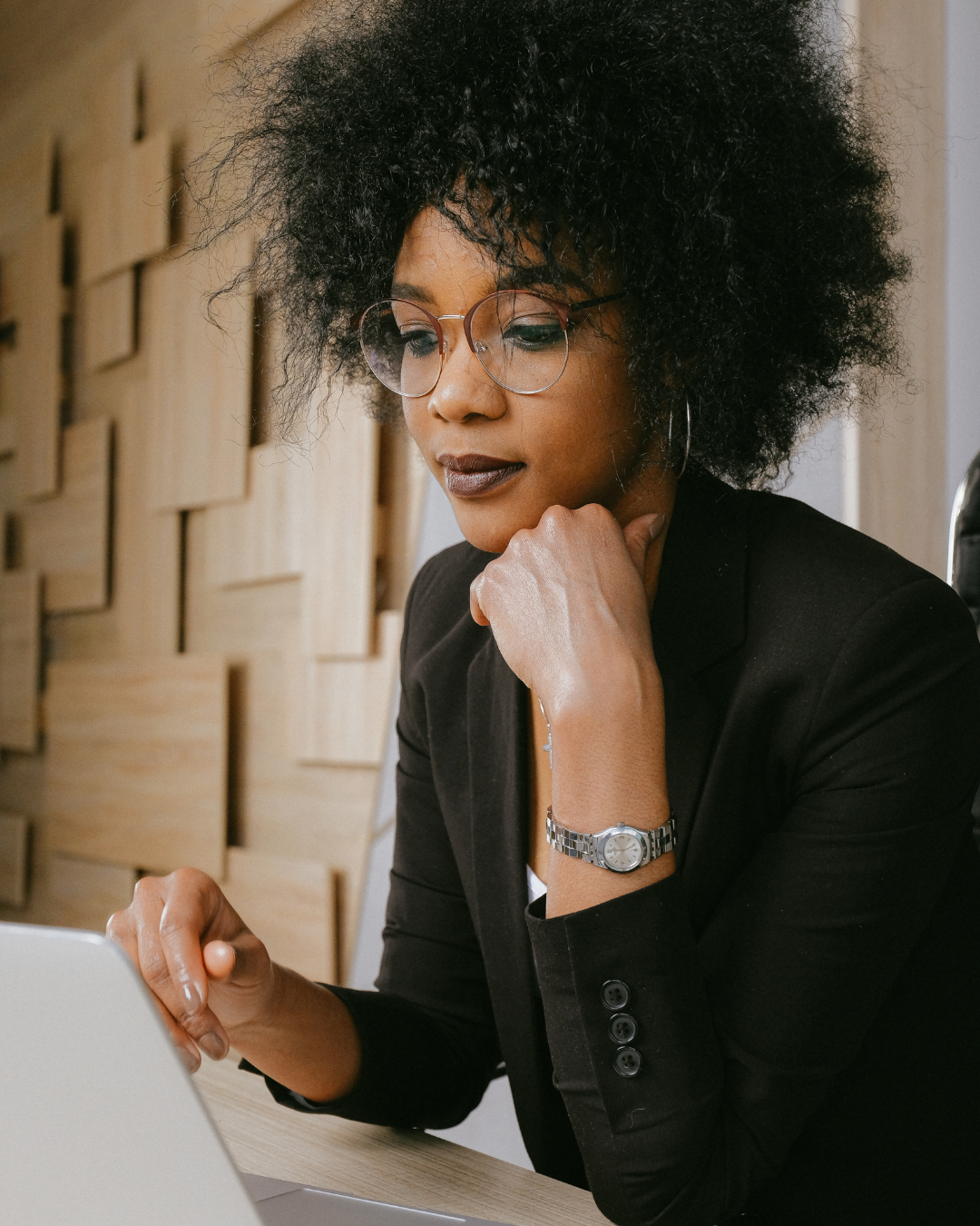 Black woman in glasses and blazer working at her laptop, focused but weary—representing high-achieving professionals quietly navigating burnout and craving balance.