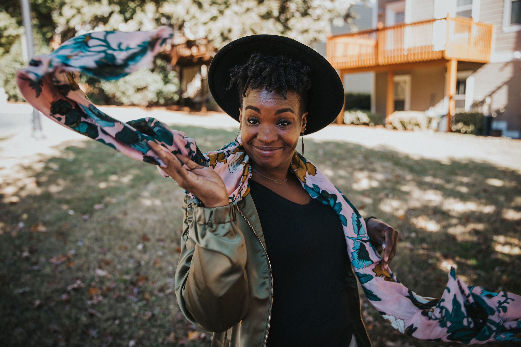 Rashidat, a mindset and lifestyle coach for high-achieving Black women, standing confidently outdoors with a joyful expression and flowing scarf — embodying soft life energy, rest-centered coaching, and empowered nervous system support.