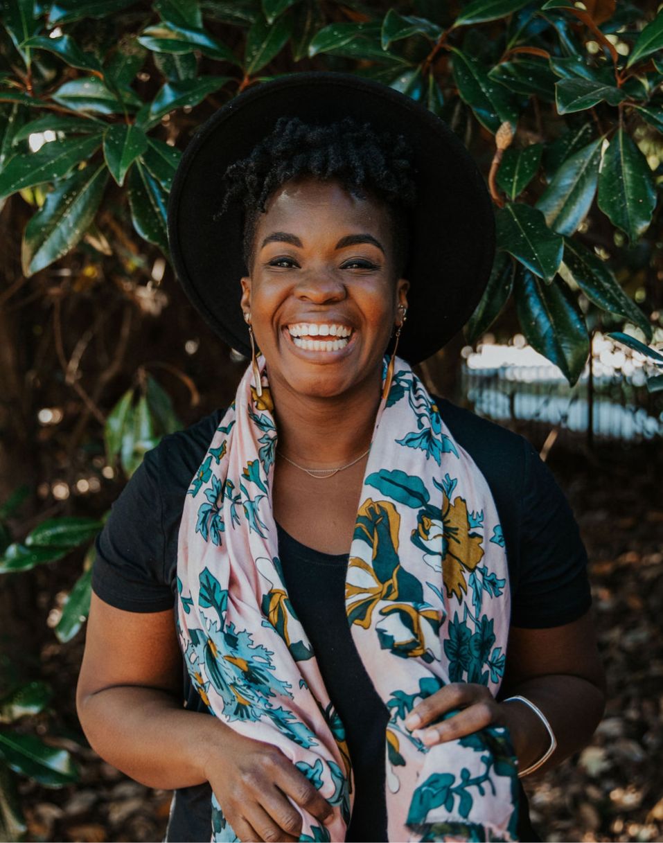 Smiling Black woman in a wide-brim hat and floral scarf standing in nature, representing the heart behind The Clarity Code soft life skills assessment. Rashidat, a certified Black life coach and mindset coach, guides ambitious women—corporate baddies, boss babes, and strong Black women—into their soft girl era through lifestyle coaching and empowerment.