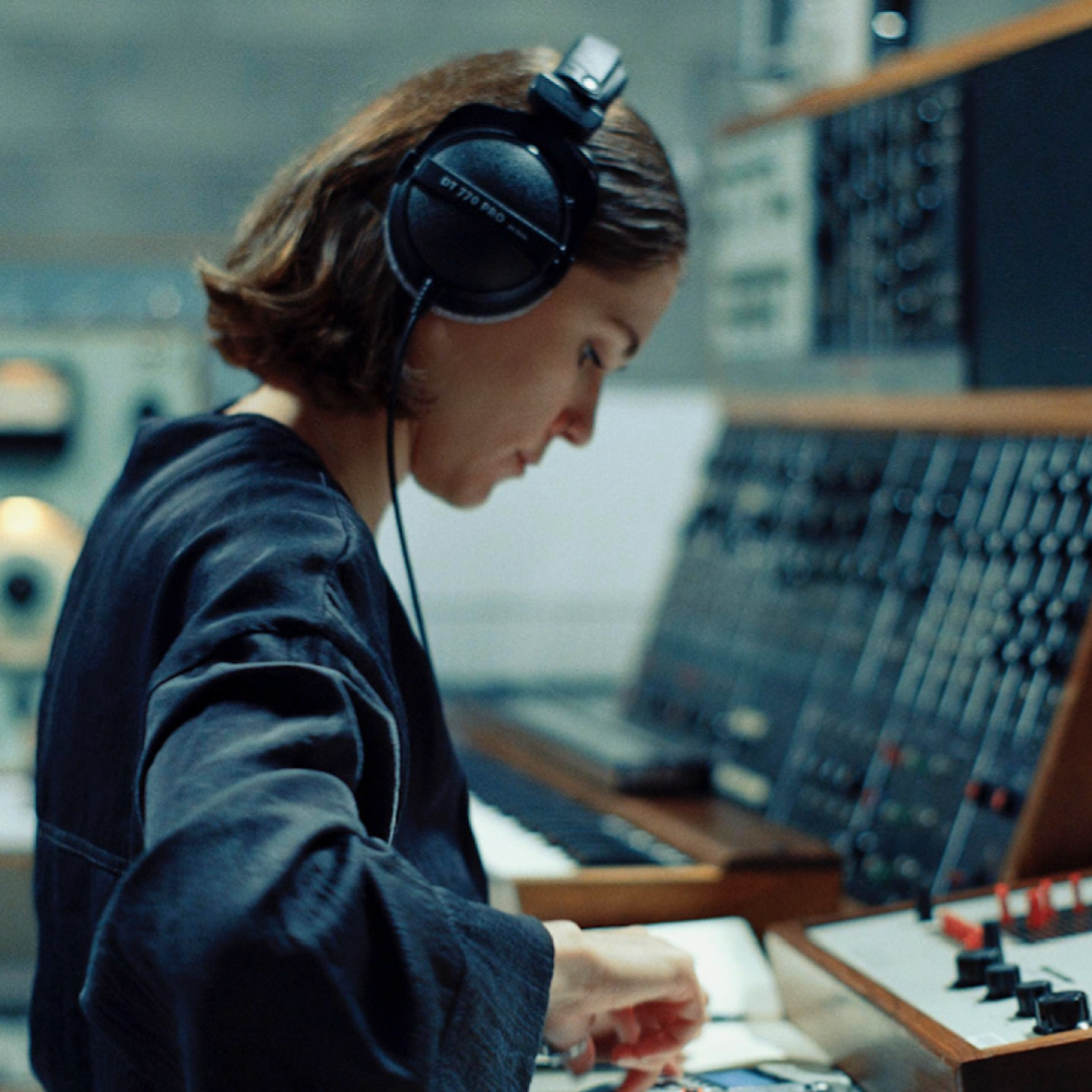 Kadr z filmu przedstawiający postać kobiecą stojącą przy mikrofonie.