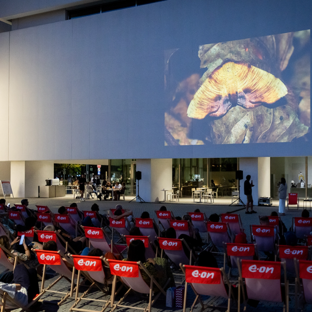 Kadr z filmu przedstawiający postać kobiecą stojącą przy mikrofonie.