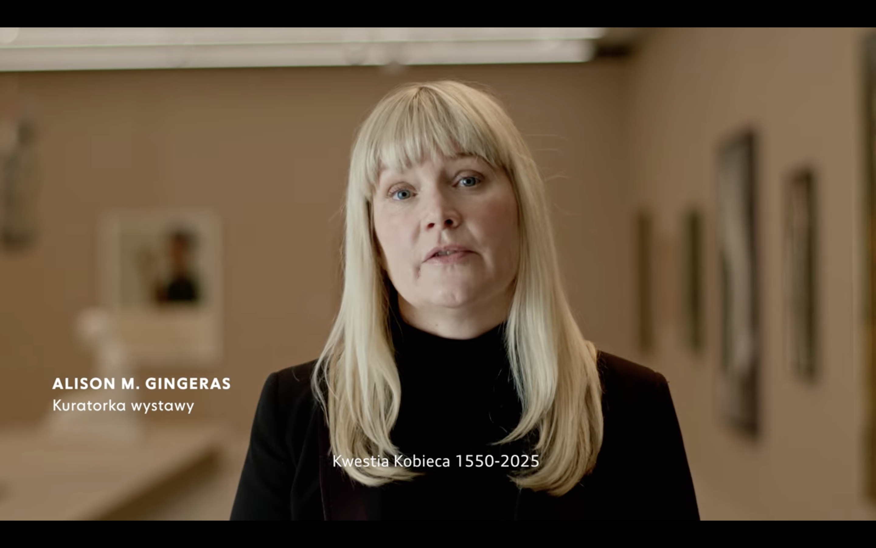 Kadr z filmu przedstawiający postać kobiecą stojącą przy mikrofonie.