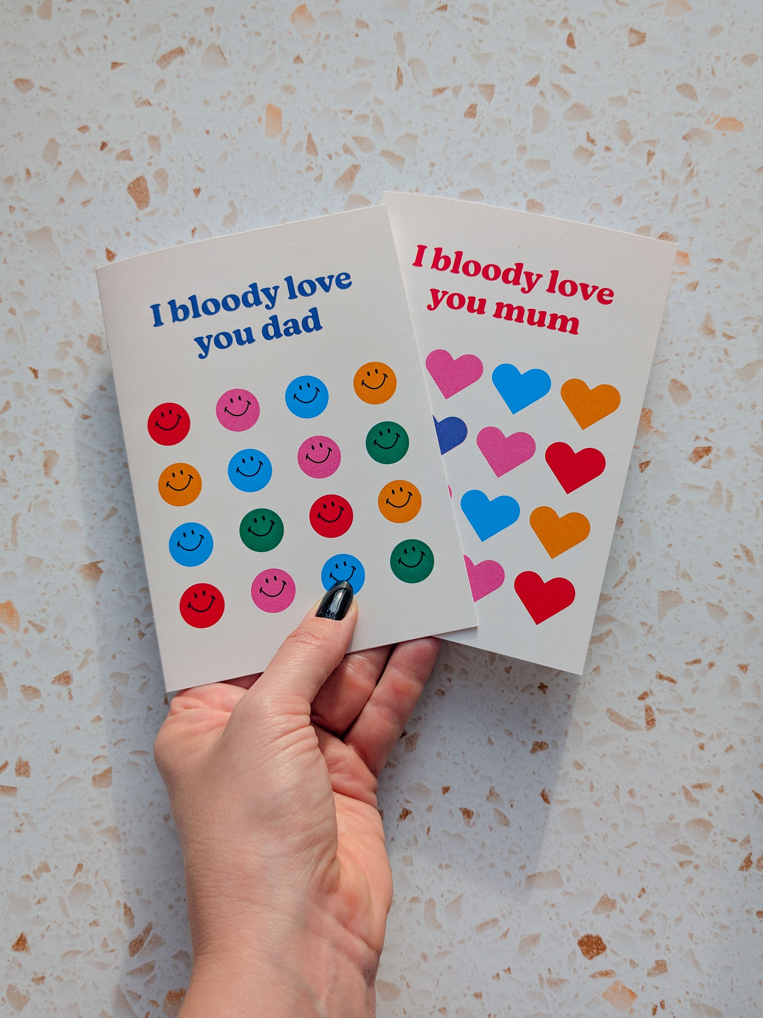 A hand holding a colourful card showing the Hove pier in front of a sunset