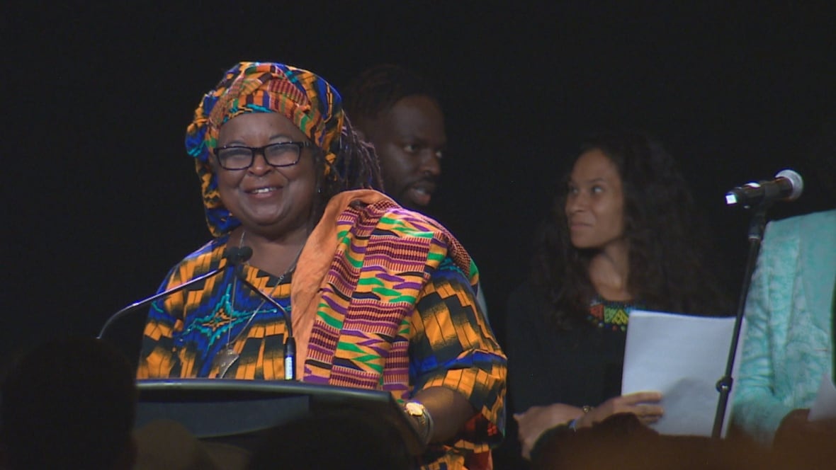 African Nova Scotian elder, Dr. Lynn Jones, smiles at a podium wearing a kente cloth head wrap.