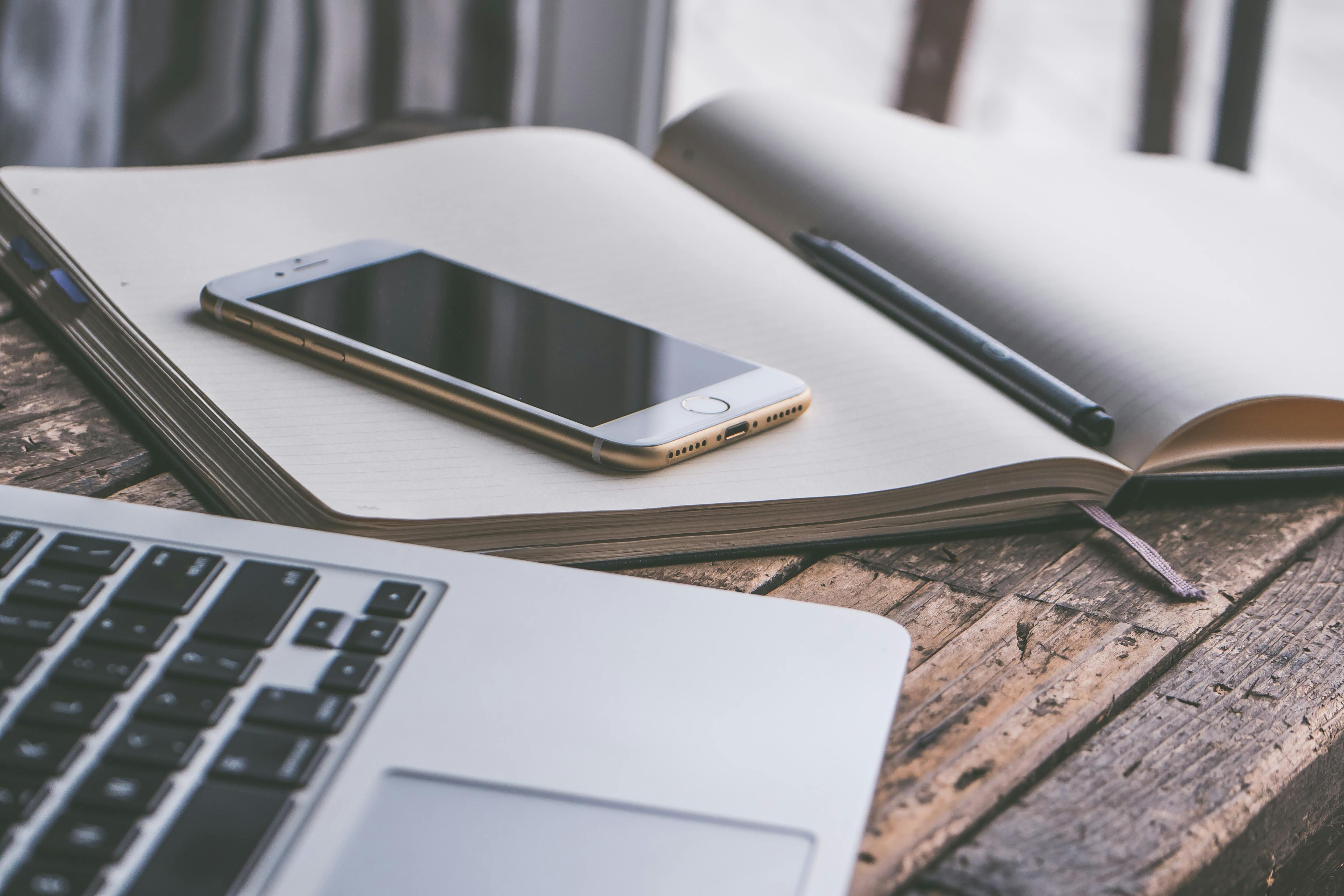 A tidy desk containing a laptop, notebook, pen and mobile phone. It is well organised.