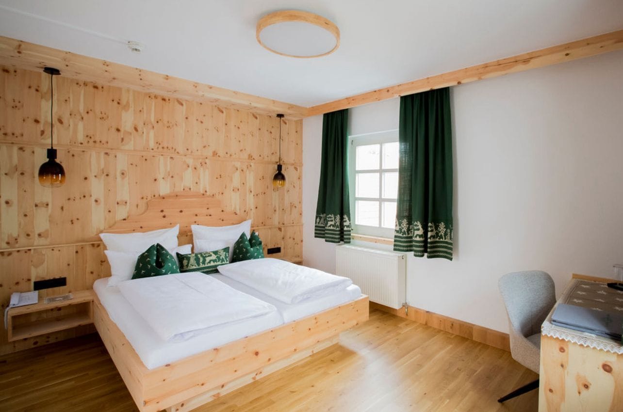 Gemütliches Zirbenzimmer im Brauhotel Weitra mit Holzbett und grünen Vorhängen