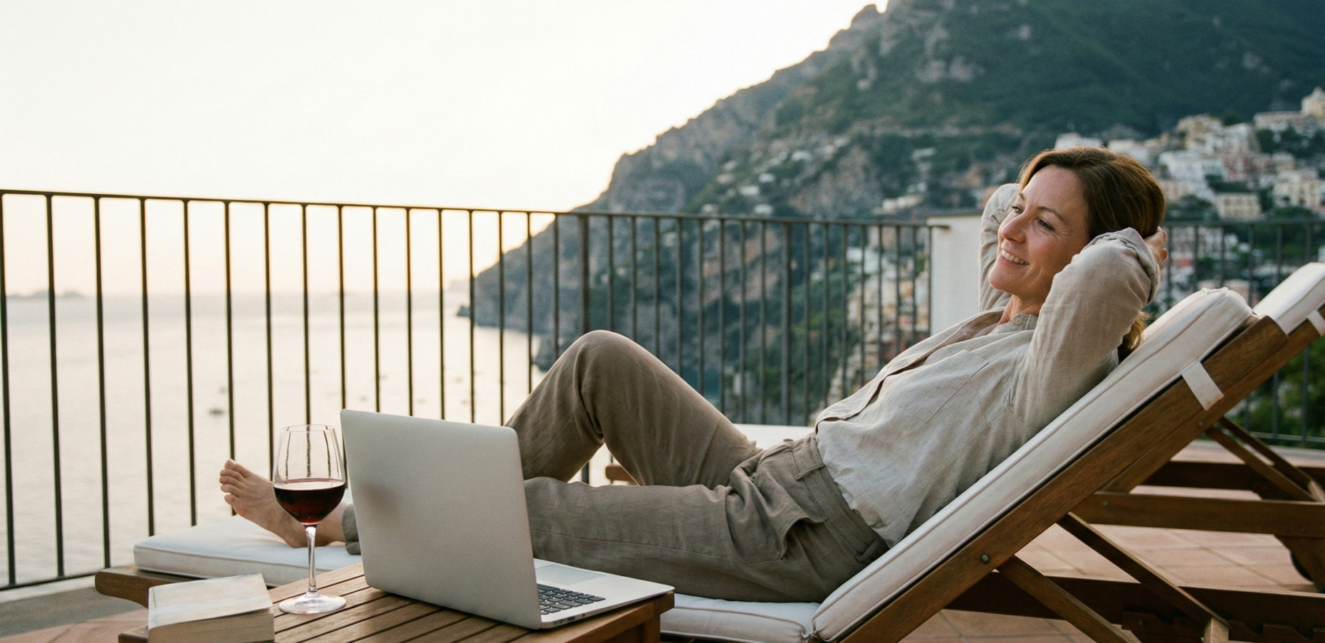 female business owner lounging on a chair overlooking the cliffs.  Her laptop and a glass of red wine is nearby.