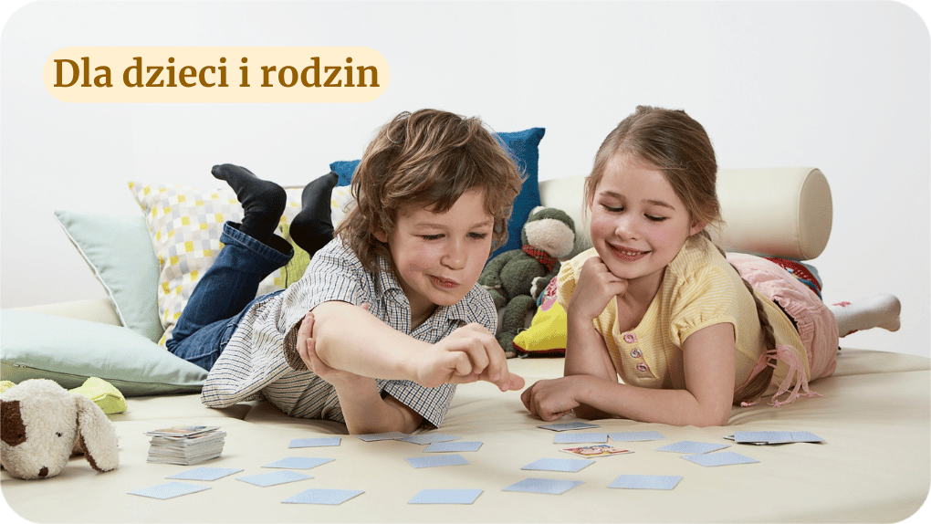 Dwójka uśmiechniętych dzieci leży na podłodze i grają w karty