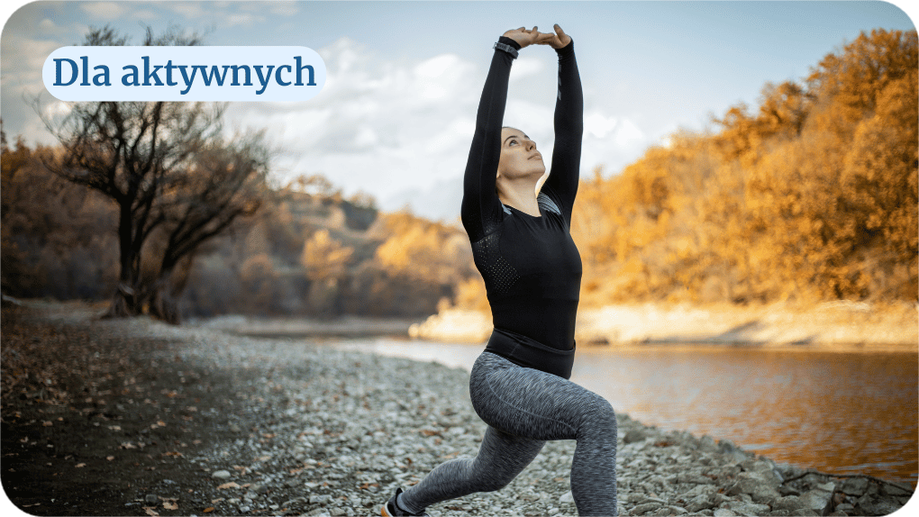 Kobieta wykonuję pozycję rozciągania na tle wzgórza oraz płynącej rzeki.