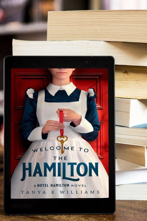 Welcome to the Hamilton by Tanya E Williams in eBook format resting against a stack of paperback books