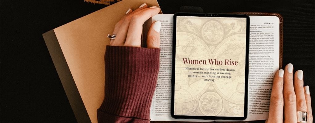 A person with manicured nails and a maroon sweater reads a book titled 