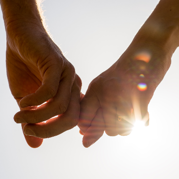 2 hands holding one another with he sunlight sparkling through the entwined fingers depicting a happy couple