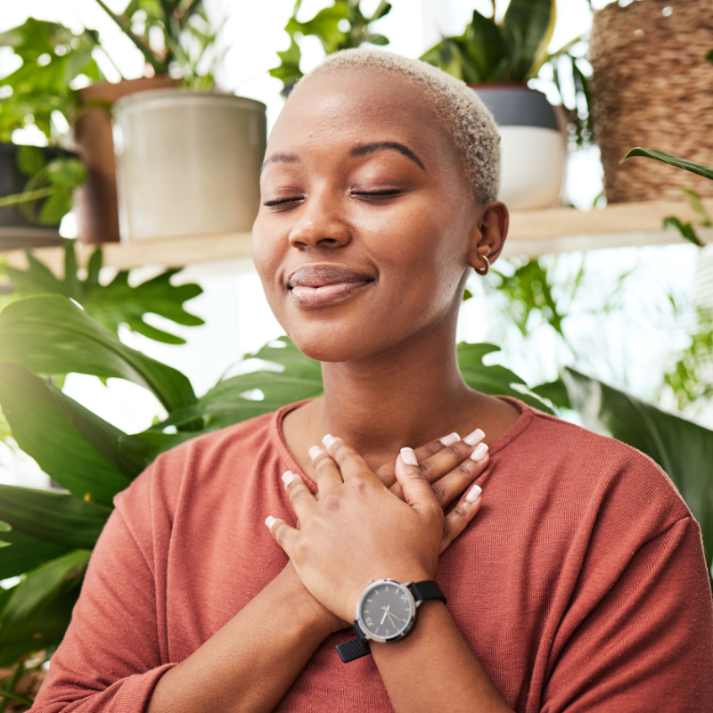young black woman holding her heart with her hands, eyes closed, smiling with a sense of inner-connection and self-love