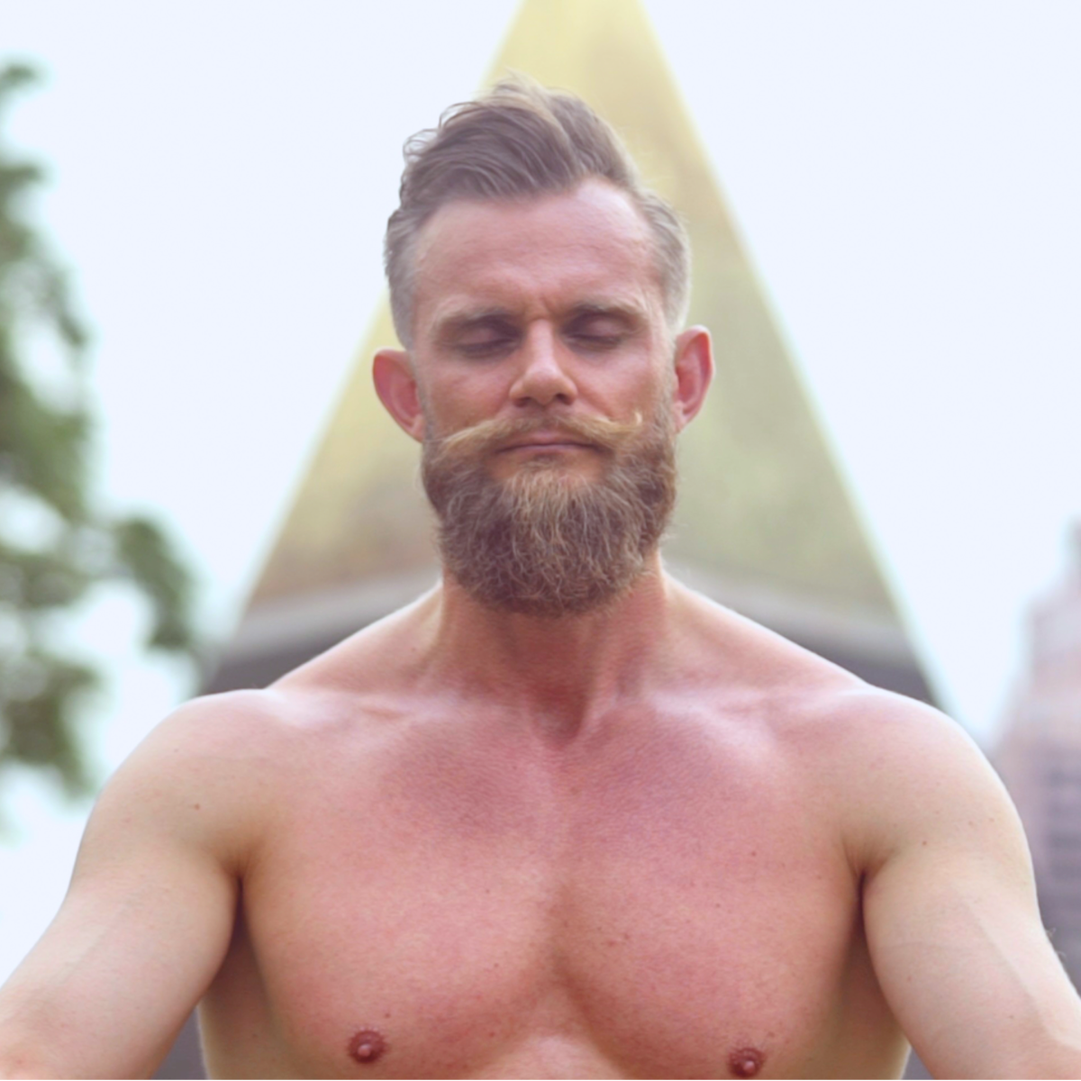 Bearded man meditating with breath-work outdoors, looking calm, connected and in peace.