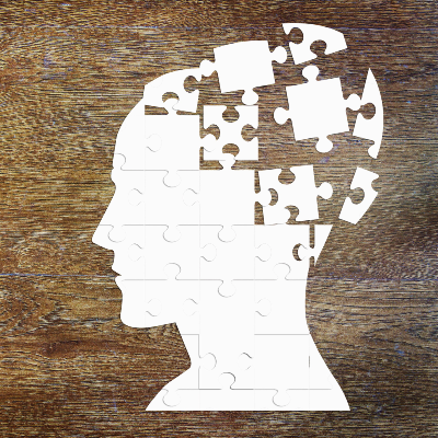 illustustration of a head made of jigsaw pieces that are scattered on a wooden surface, depicting the piecing back together of the mind for mental health