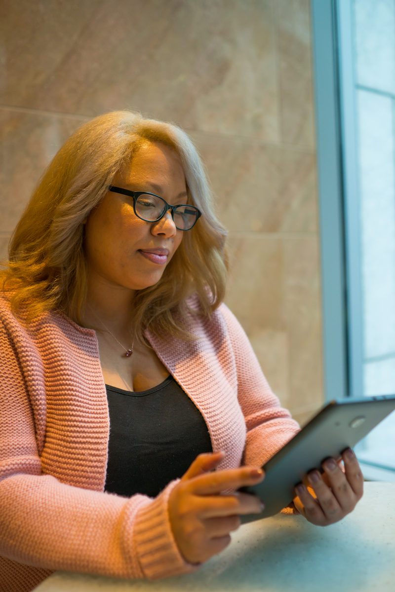 Image of a larger-bodied Black feminine-appearing person smiling into a tablet during telehealth therapy