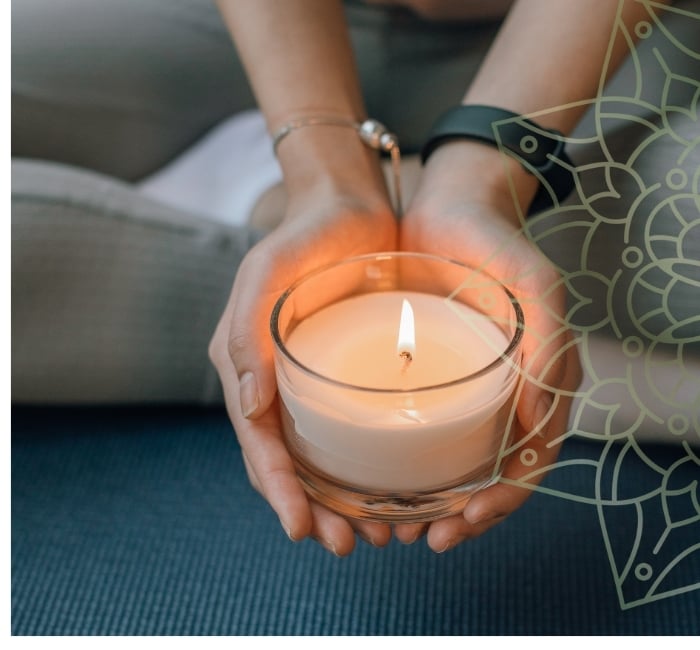 A person holding a candle cupped in her hands with a mandala image overlay.