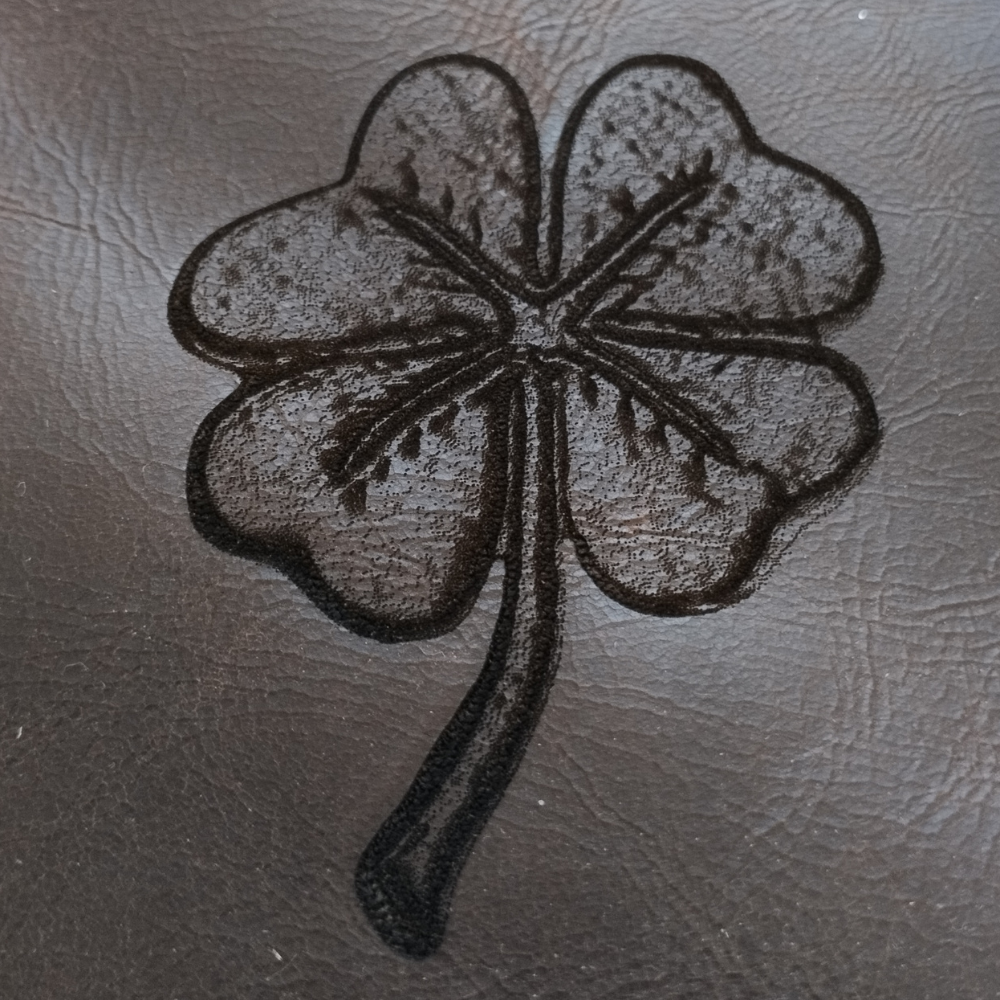 Engraved leather piece with four-leaf clover design, handcrafted lucky charm leather artwork with rustic finish