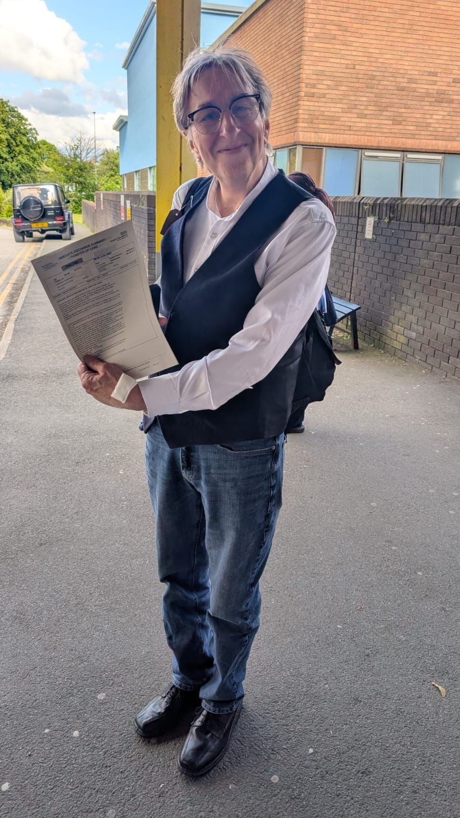 Alan Miles, smiling and posing with a document, outside ... where?