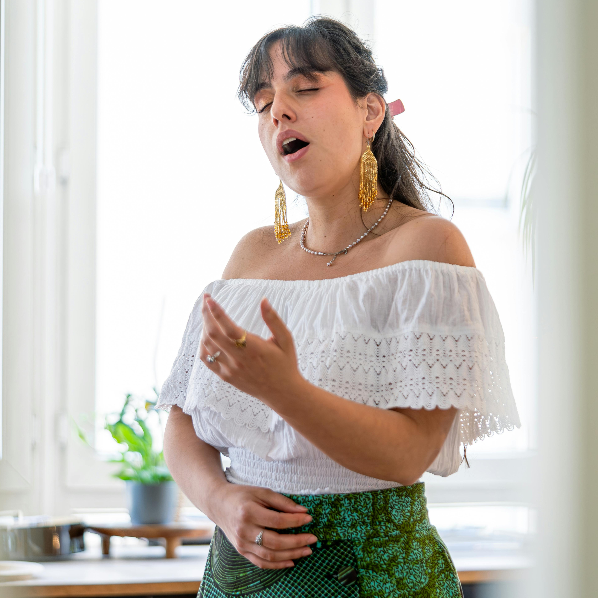 Female singer performing passionately with eyes closed, demonstrating vocal expression and technique in a light-filled room.