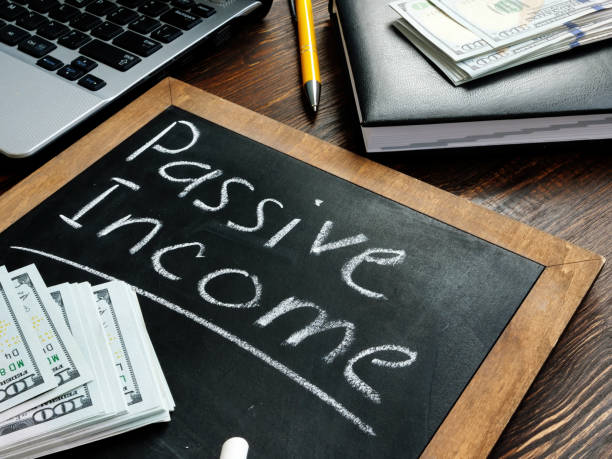 Passive Income and residual income written with white chalk on a chalkboard with a stack of money on it.