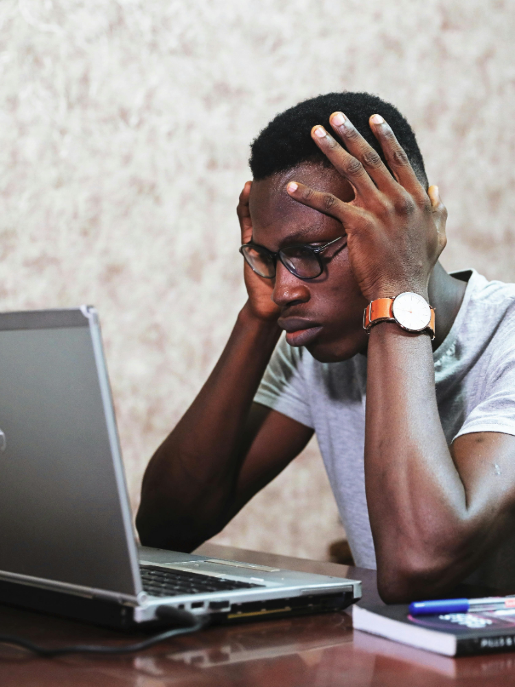Photo by Oladimeji Ajegbile. Black man holds head in frustration by laptop.
