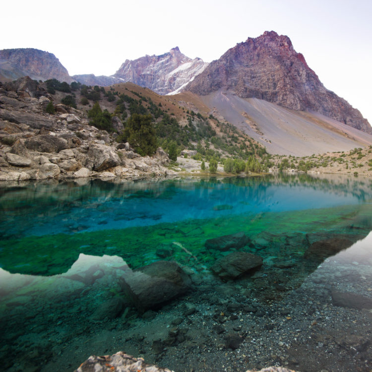 A crystal-clear mountain lake with vibrant turquoise and green hues reflects the rocky peaks and sparse forest surrounding its shore.