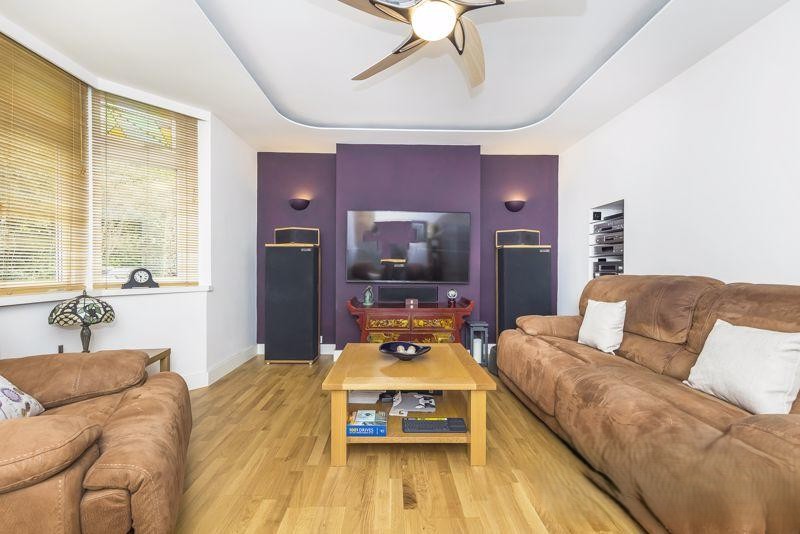 Lounge room with sofas and armchair in brown suede effect, media storage for audio and tv equipment. Hidden storage. Ceiling light raft with decorative ceiling rose left visible. Wooden oak floor