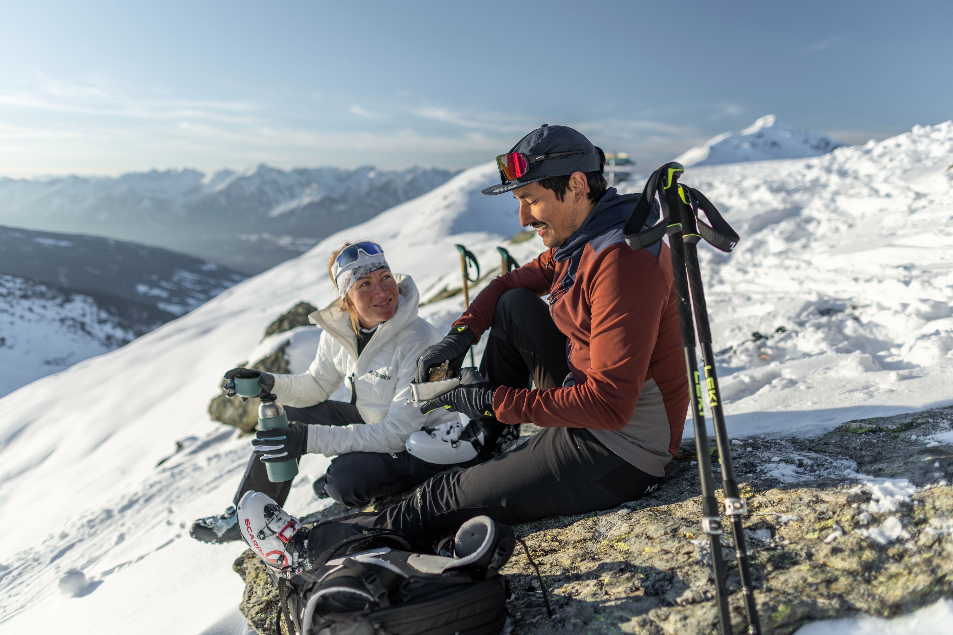 Two hikers with LEKI walking poles resting on a snowy summit