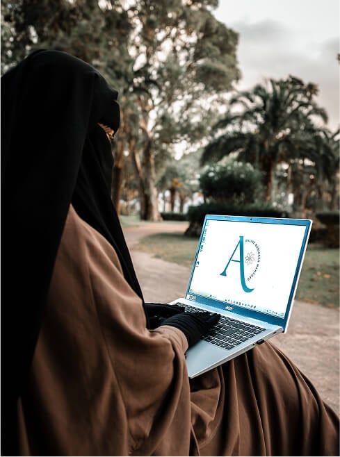 image of Alina wearing niqab (veil) sitting on a bench at a park with a laptop on her lap, typing