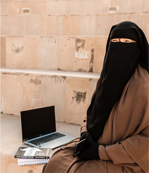 image of a muslim woman wearing niqab (veil) looking to the left thoughfully with a backdrop of palm trees and a Moroccan style building