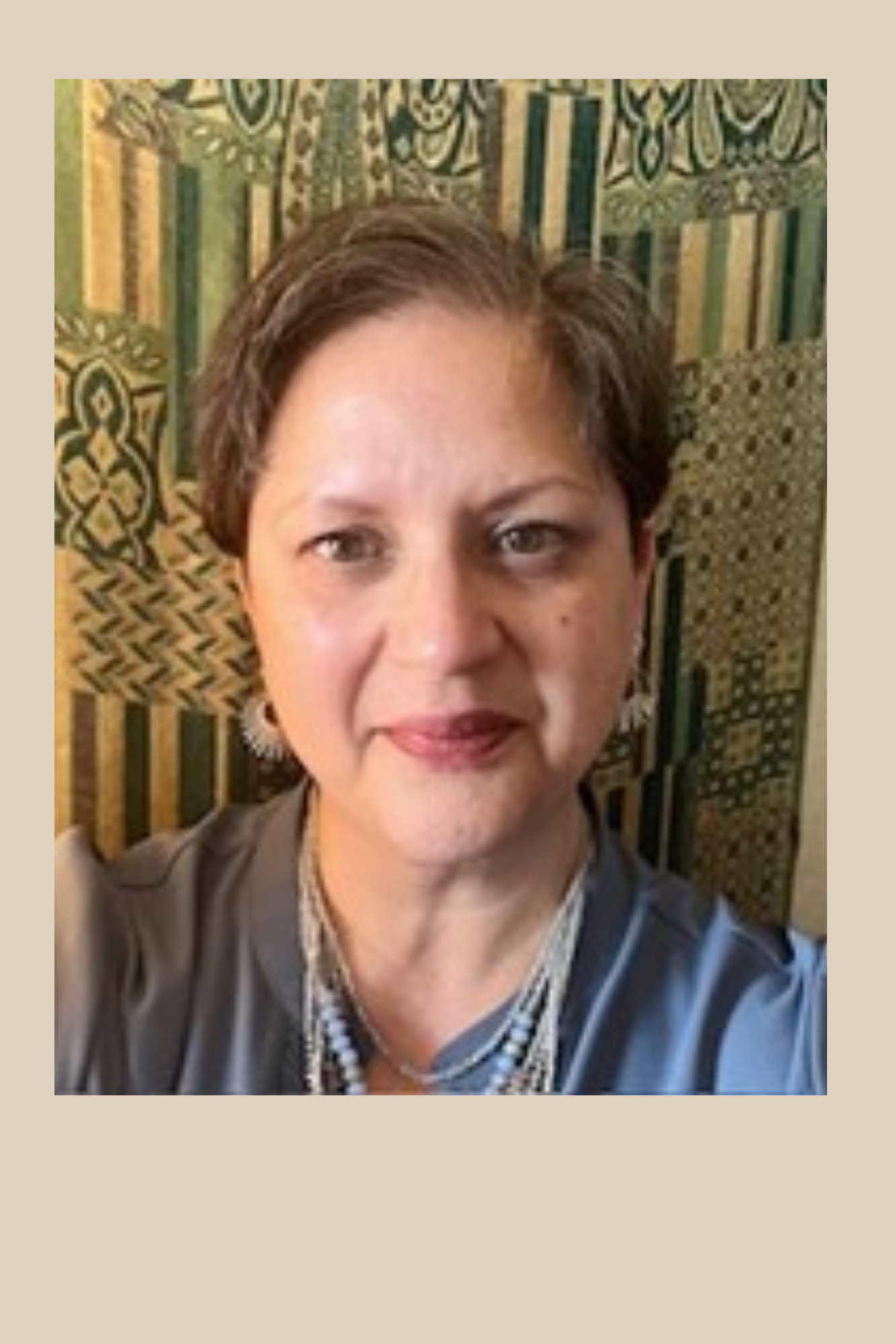 Headshot of Becky Thomas. middle aged woman with short brown hair. wearing earrings. Standing in front of a tapestry.