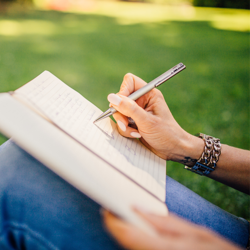 Person writing in notebook outdoors - guided writing workshop for Letter of Wishes