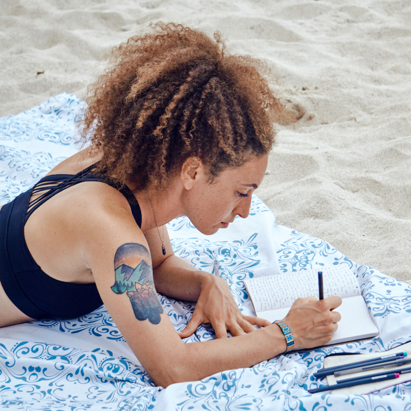 Woman writing in journal on beach - who the Legacy Letter Writing workshop is for