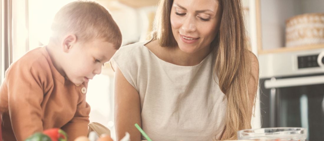 A mother and her toddler cooking together at the kitchen counter
