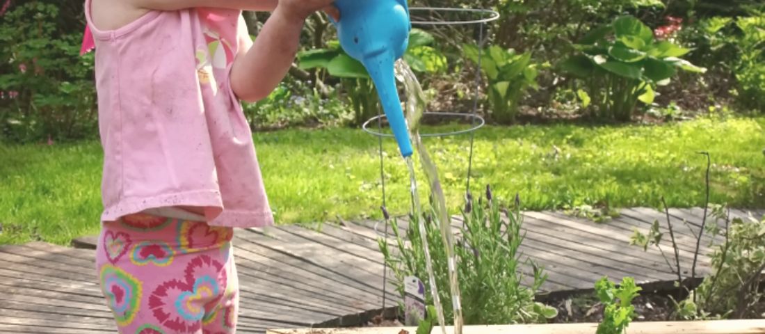 A little girl watering a raised garden bed