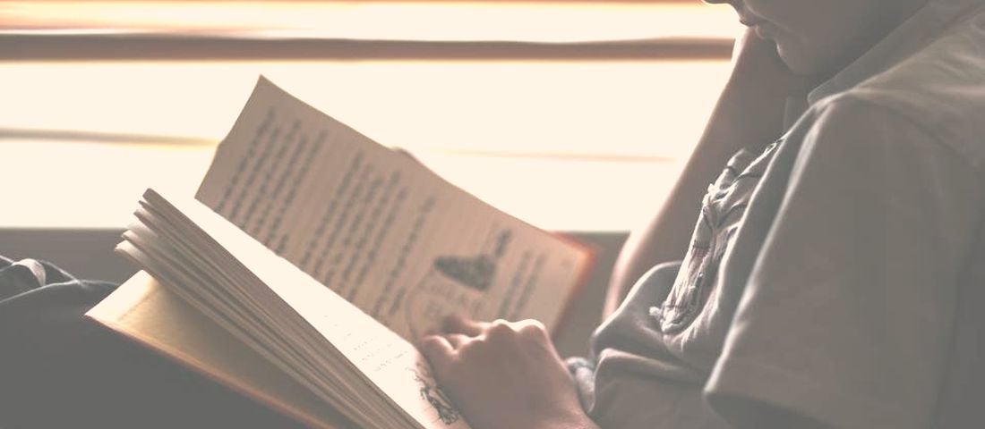A child reading an open book in soft window light