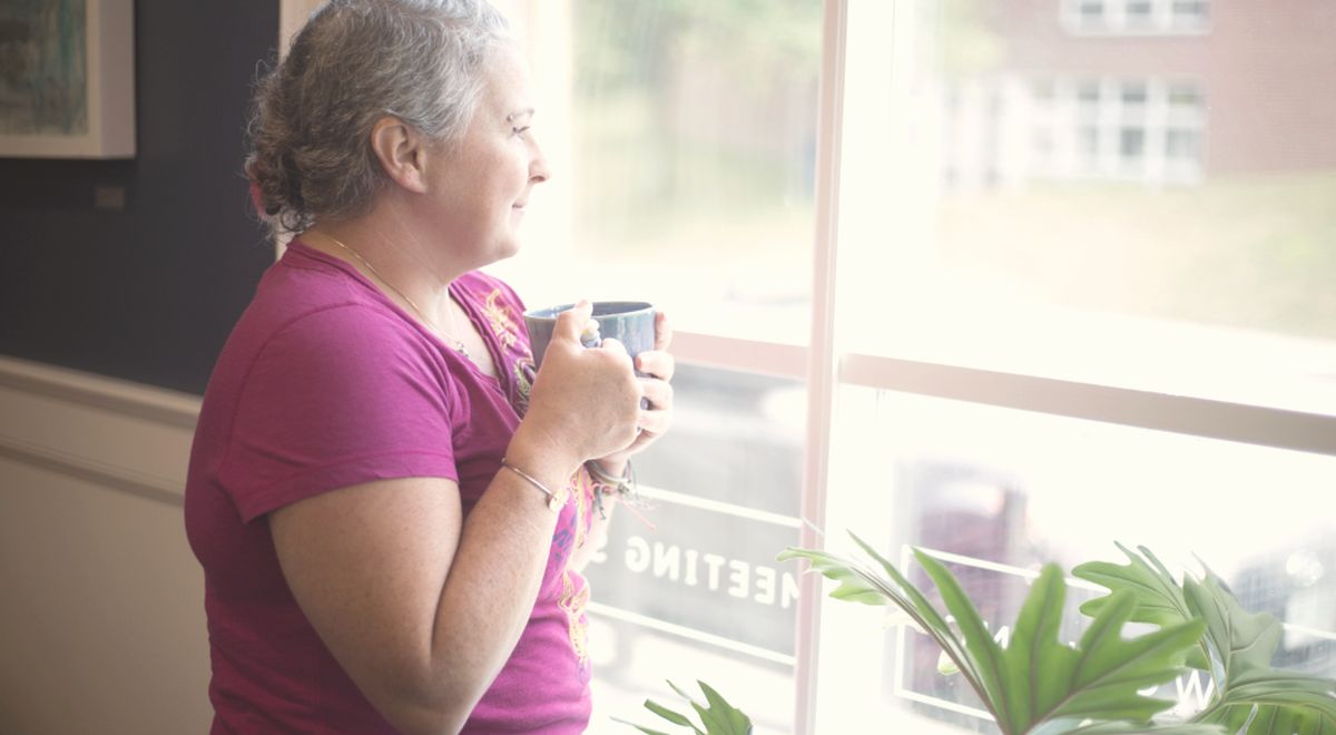 A woman holding a warm mug, looking out a bright window