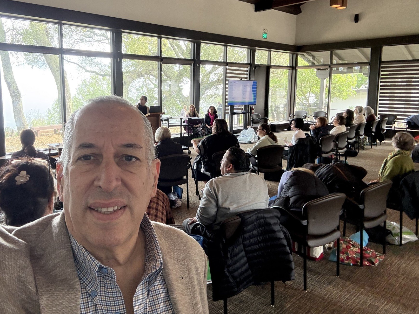 Joel Barnehama taking a selfie with wellness retreatants in the background listening to another presenter