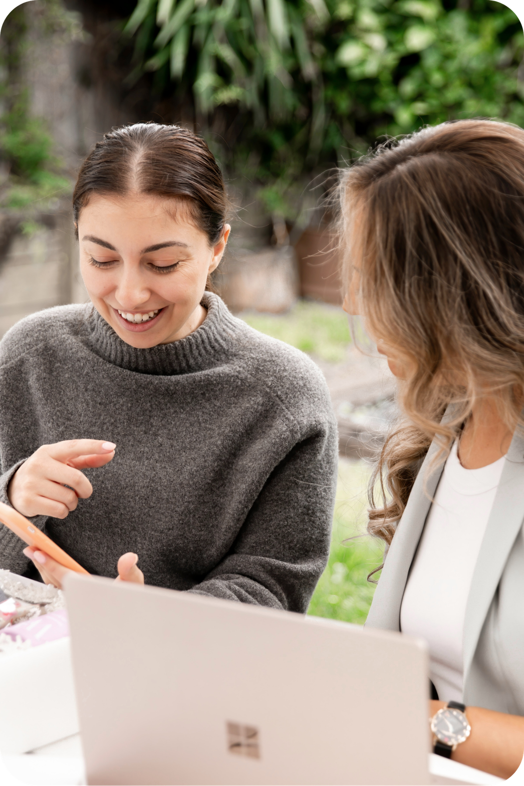 two women sitting at table looking at information on a phone