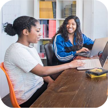 Farhana Aboo in a coaching conversation with a client, sitting at a desk in a relaxed, informal setting