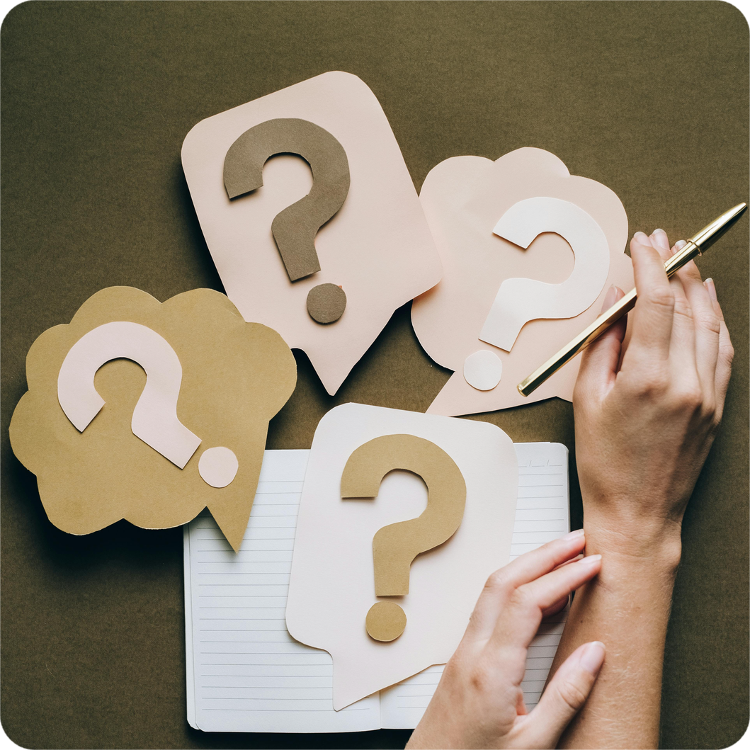 A hand holding a pen near a notebook, surrounded by floating question marks, symbolising clarity and self-reflection through coaching