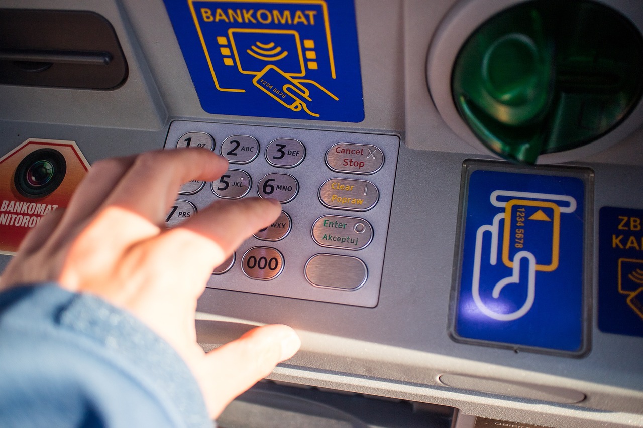 Person covering ATM keypad while entering PIN to prevent skimming or hidden camera fraud