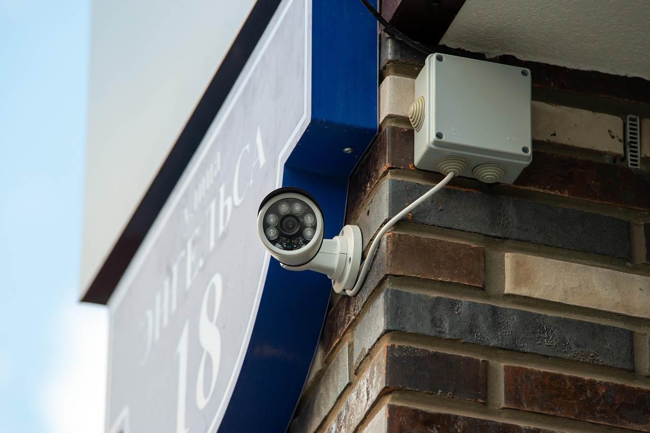 Outdoor security camera mounted on a brick wall near the entrance, overlooking the street and front door.