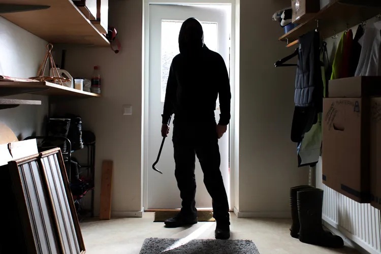 Hooded burglar with crowbar entering a home through the front door