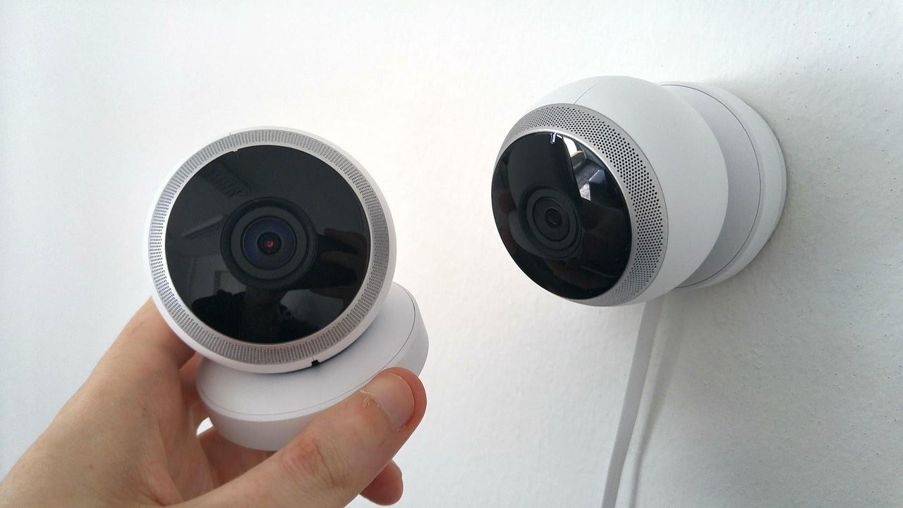 Two indoor dome security cameras, one being held and one mounted on a white wall.