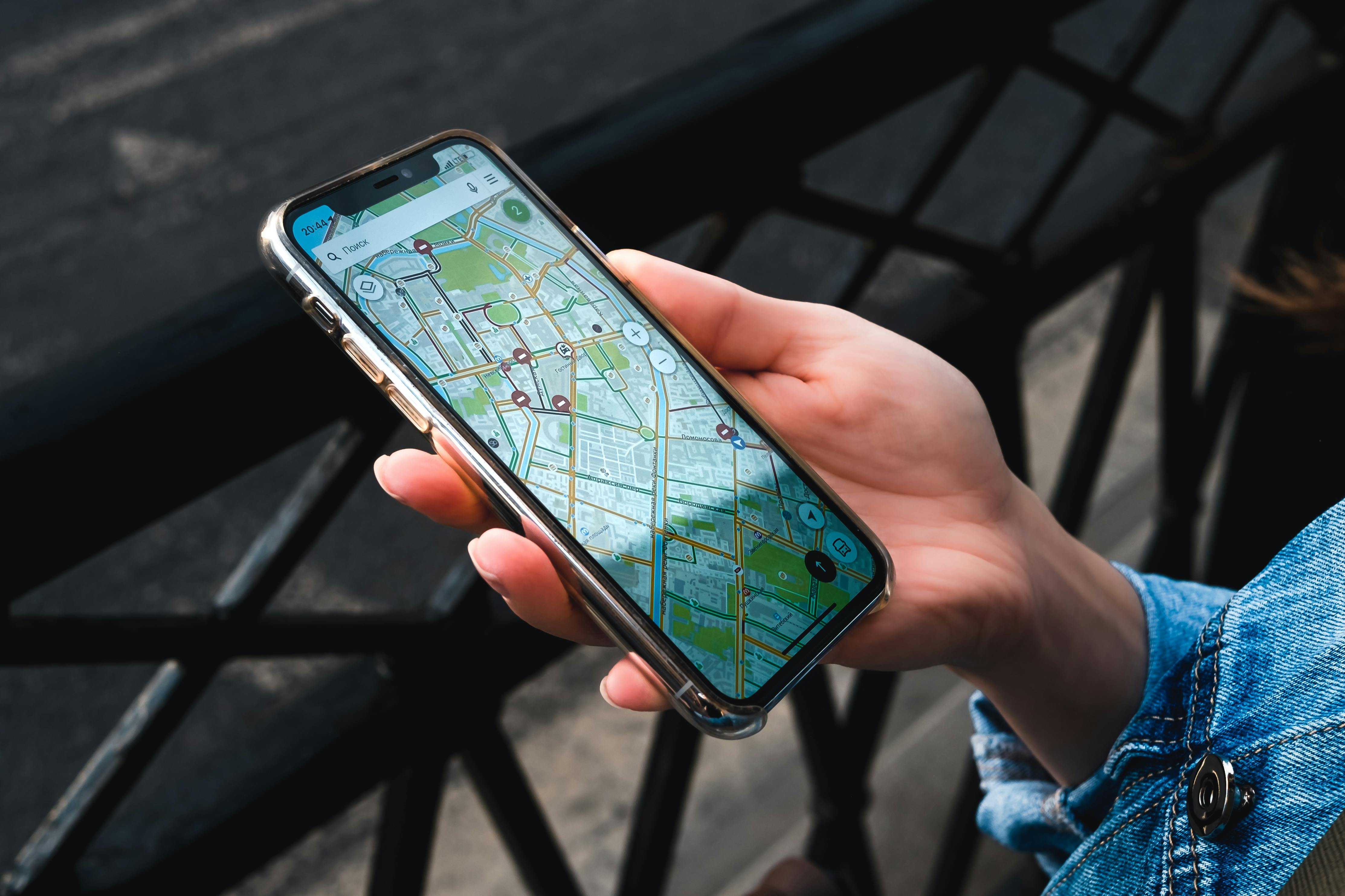 Hand holding smartphone showing map while standing near railing outdoors