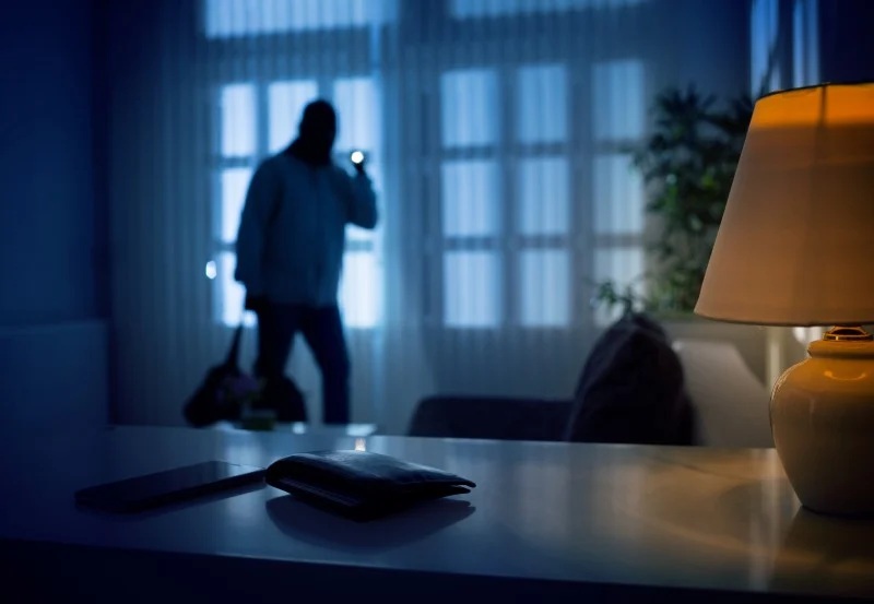 Burglar searching a dark home with a flashlight, viewed from behind a window