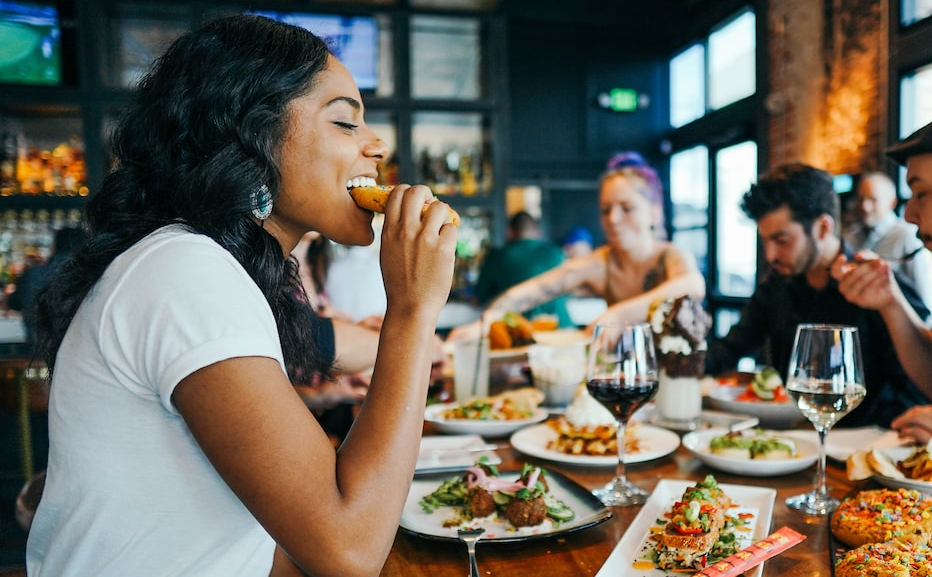 Mujer comiendo en un restaurante acompañada de amigos